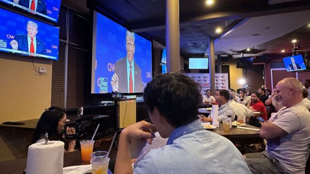 people watch the donald trump on a screen at a bar
