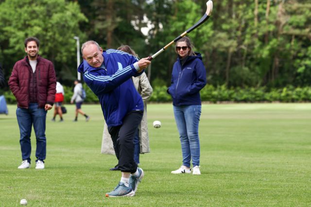 Ed Davey playing shinty in Scotland, he is swinging a stick