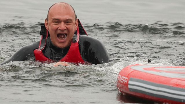 Ed Davey wearing a life jacket in water next to a paddleboard