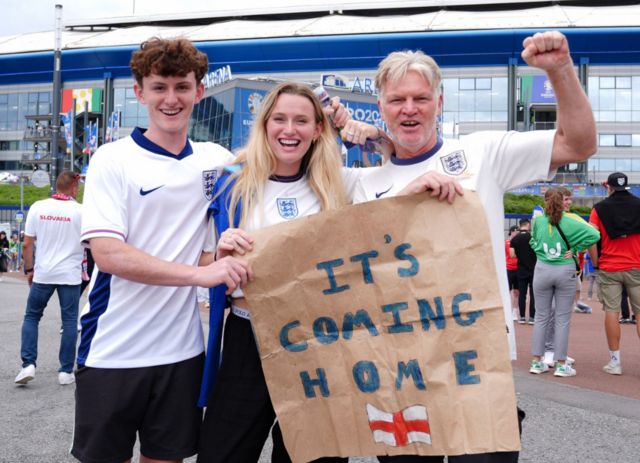 England fans with a sign that reads "It's coming home" pose for photos outside the Arena