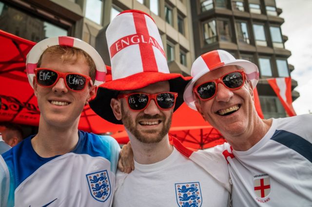 Three England fans wear their England shirts and sunglasses