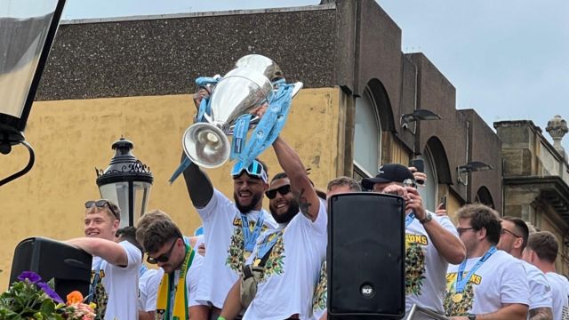 Smiling Saints players on the top deck of the bus with the trophy