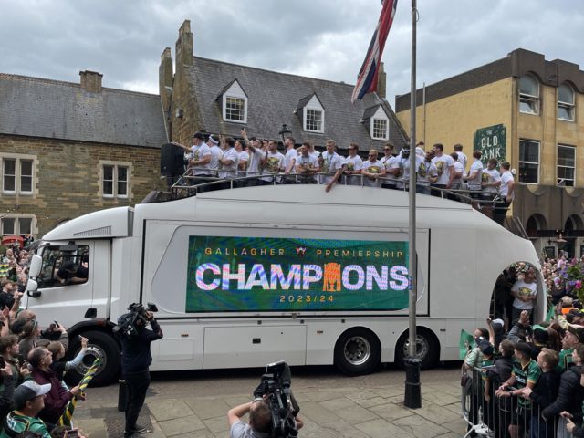The Northampton Saints line up on top of the team bus, as crowds cheer