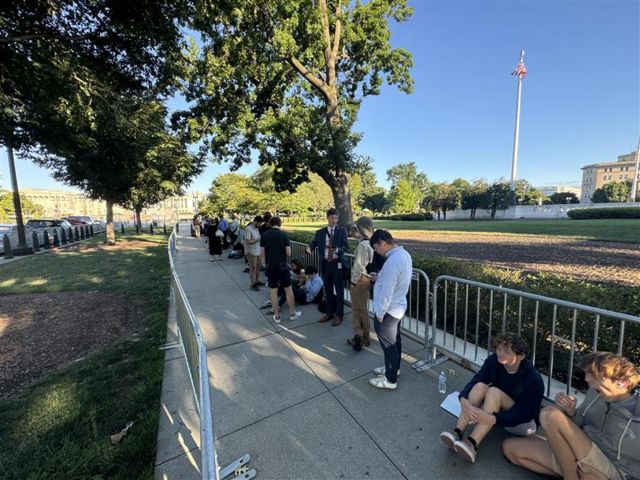 People lined up on sidewalk between security barriers