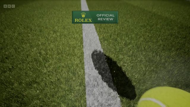 The shadow of a tennis ball is shown on a white line with a yellow ball flying towards the camera