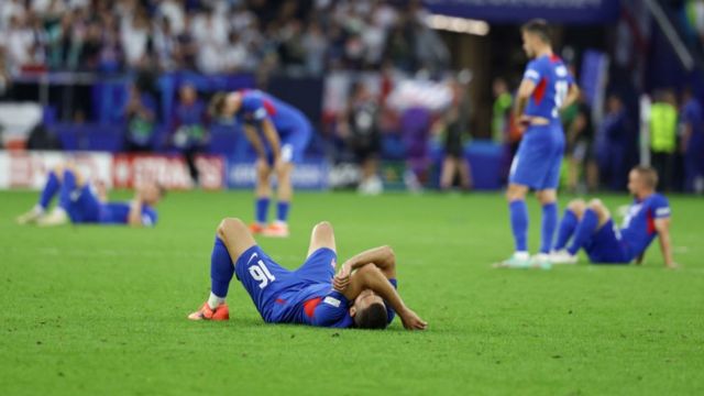 Slovakia players are all on the floor after defeat to England during Euro 2024.  One player is laying down with his arm over his eyes.