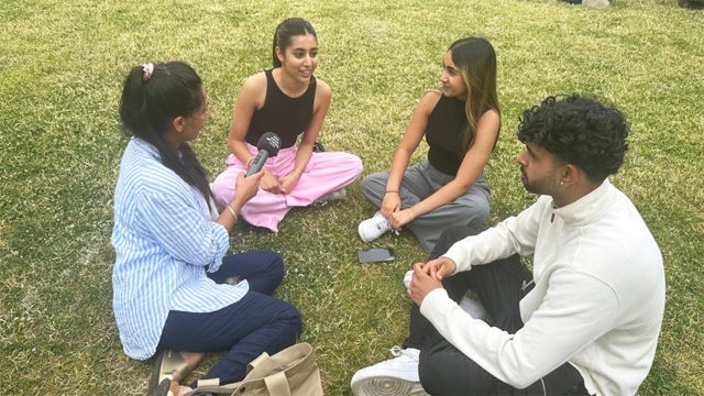 Four people sitting in a circle on green grass during an interview