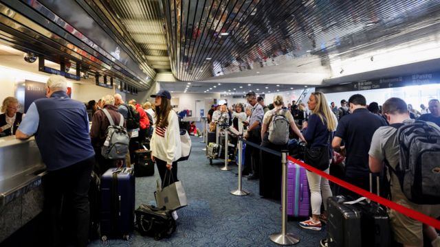 People stand queuing at desks with airport staff stood behind them