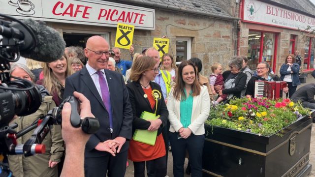 SNP Leader and First Minister John Swinney and Deputy First Minister Kate Forbes standing outside a café.