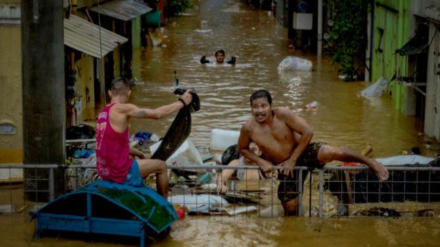 Residents climb a fence in a flooded road caused by Typhoon Gaemi and monsoon rains on 24 July in Manila