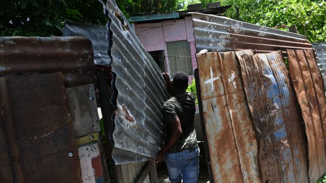 A man carries plates to protect the roof of his house as Hurricane Beryl moves towards Jamaica