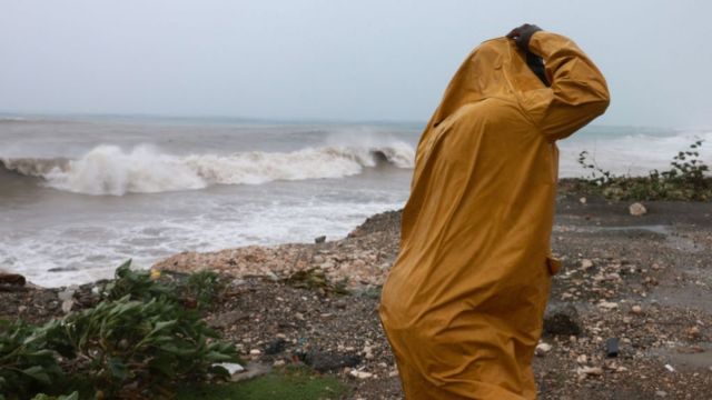A person stands in the wind and rain as waves crash ashore as Hurricane Beryl spins offshore on 3 July 2024