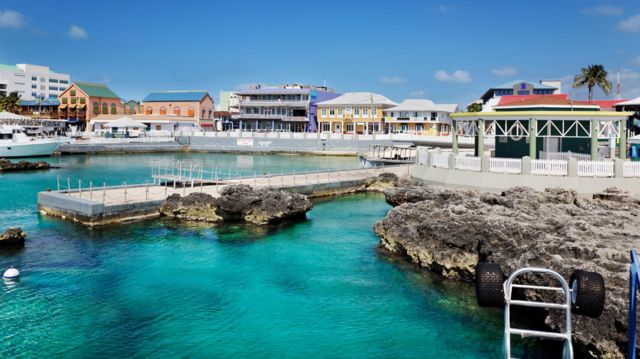 The capital of the Cayman Islands, Georgetown, with blue waters and white and orange buildings on the shoreline where small boats dock