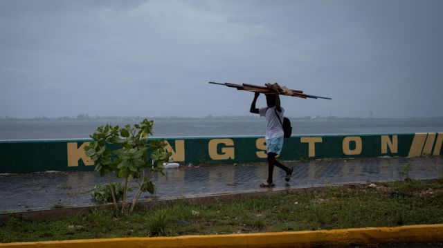 A man walks down a pavement carrying wood on his head as Hurricane Beryl approaches, in Kingston, Jamaica.