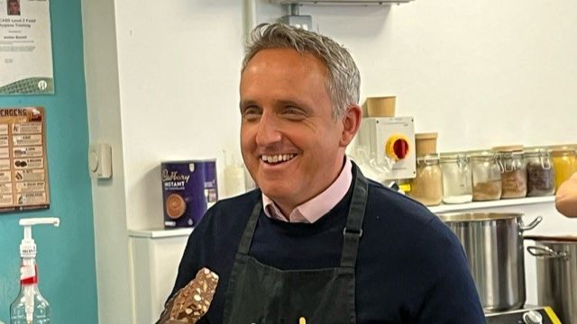 Alex Cole-Hamilton wearing an apron and holding a brownie in a pair of tongs