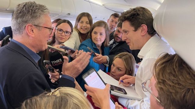 Reporters huddle around Keir Starmer on board an airplane