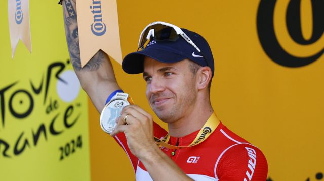Dylan Groenewegen holds his medal aloft on the podium after winning stage six of the 2024 Tour de France