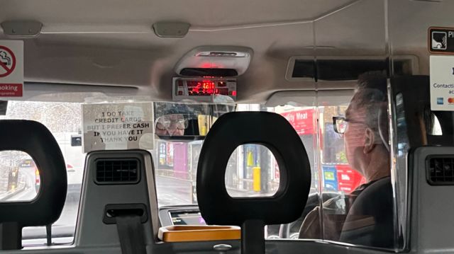 Ronnie the taxi driver in the front of his cab talking to BBC reporter Adriana Elgueta