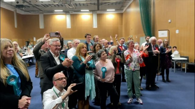 People holding up mobile phones and celebrating at one of the Cumbria counts