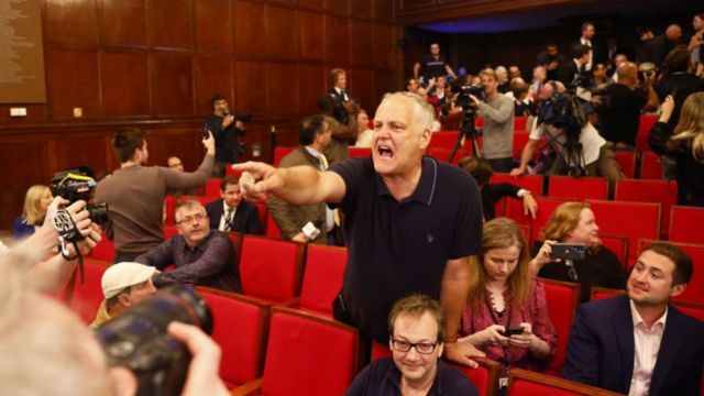 A man shouting and pointing his finger in a theatre.