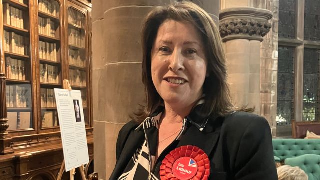 Barrow's Labour candidate Michelle Scrogham wearing a black suit, patterned shirt and a red rosette