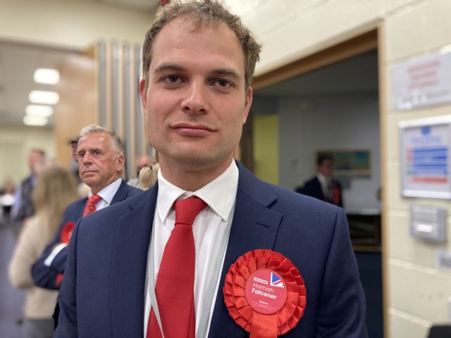 Hamish Falconer at the election count wearing a red tie and rosette