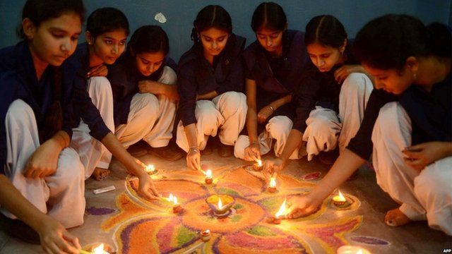 Indian school girls lighting candles as they sit near a "Rangoli", which is made out of coloured powder during pre Diwali celebration at a school in Amritsar