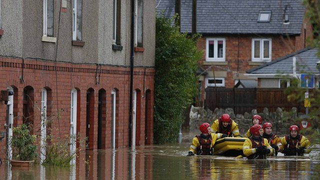 Firefighters pull a boat as they wade down a flooded street in St Asaph