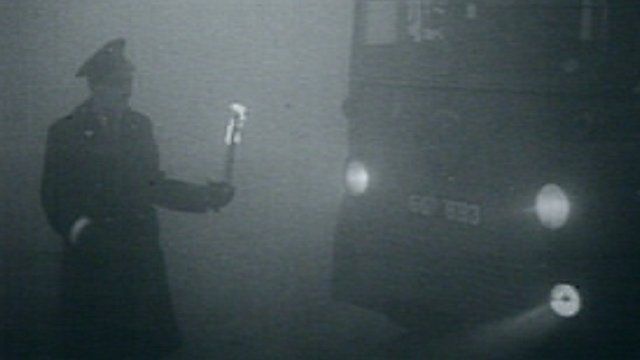 A policeman directs a bus with a flame during the Great Smog