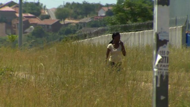Woman walks down South Africa street lined by tall grass