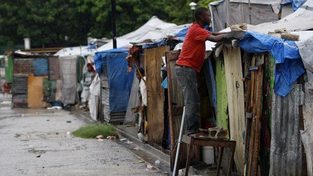 A Haitian earthquake survivor reinforces his tent, under the rain, at a provisional camp