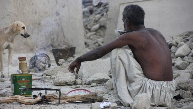 A survivor of an earthquake sits as he takes tea on the rubble of a mud house after it collapsed following the quake in the town of Awaran