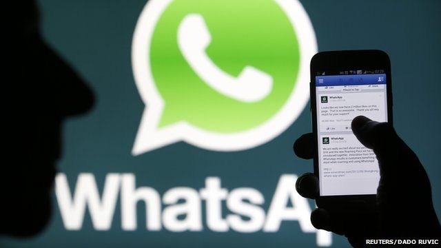 Shadow of person holding phone using WhatsApp in front of WhatsApp logo