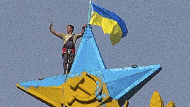 A man takes a "selfie" as he stands with a Ukrainian flag on a Soviet-style star