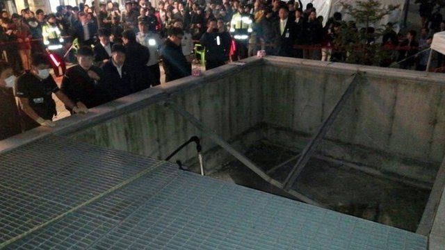 People gather around a collapsed ventilation grate at an outdoor theatre in Seongnam, south of Seoul, South Korea, Friday, Oct. 17, 2014.
