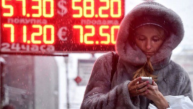 A woman walks past a board listing foreign currency rates against the Russian ruble in central Moscow