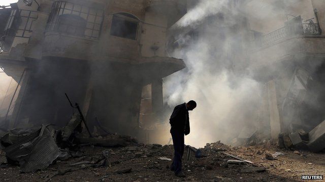 A man (with head bowed) walks in front of a burning building after a Syrian Air force airstrike in Ain Tarma neighbourhood of Damascus in this January 27th 2013