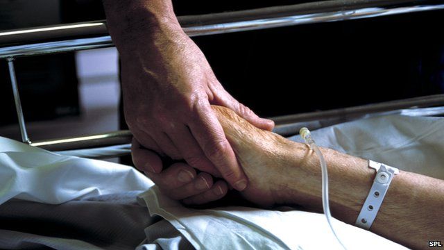 Close up of hand holding the hand of an elderly patient with an IV drip