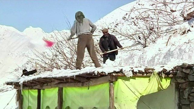 Residents shovel snow off of a roof