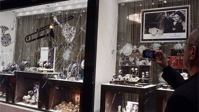 A man takes a picture of a broken shop window of a jewellery shop, which was damaged by demonstrators in Athens on 26 February