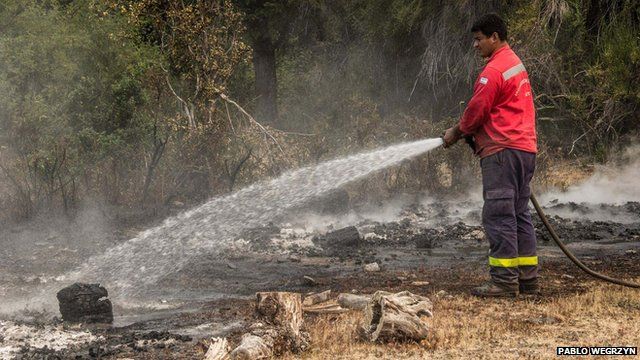Man training water hose on burning ground in Patagonia National Park