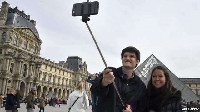 Tourists use a selfie-stick to take a picture of themselves outside the Louvre in Paris