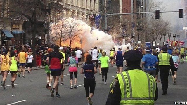 Runners continue to run towards the finish line of the Boston Marathon as an explosion erupts near the finish line of the race