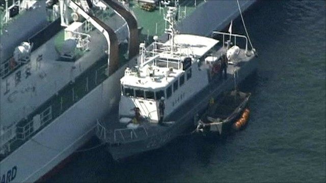 Refugees' small wooden boat tied to Japanese coastguard boat, tethered to large coastguard ship