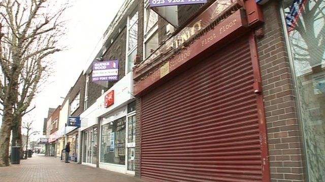 Row of high street shops, one with the shutter drawn down.