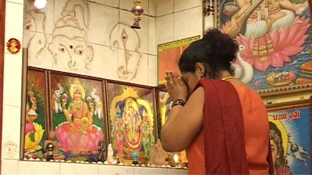Woman prays before framed Hindu deities.