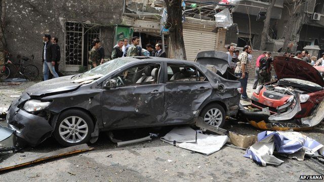 Photo released by the Syrian official news agency SANA, shows Syrians inspecting a damaged car at the scene of a car bomb attack near the Sabaa Bahrat Square