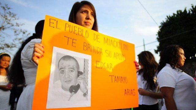 A woman in Mexico holds up a sign showing a photo of Edgar Tamayo Arias