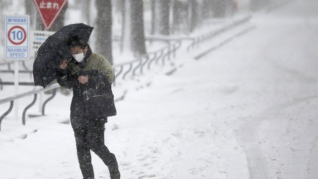 A man walks against a snowstorm on a snow-covered road in Yokohama, Japan