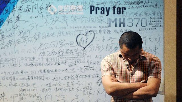 man stands in front of a billboard in support of missing Malaysia Airlines flight MH370